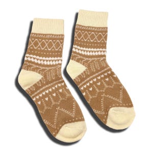 May include: A pair of crew-length socks featuring a tan and cream colour palette. The socks display a repeating pattern of white geometric lines, small heart shapes, and zig-zag motifs, with solid cream-coloured cuffs, heels, and toe sections.