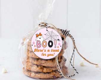 May include: A stack of chocolate chip cookies inside a clear plastic bag, tied with twine and a round tag. The tag features a ghost with an orange bow, a spider web, a small spider, and the text "BOO! Here's a treat for you!" in pink and orange.