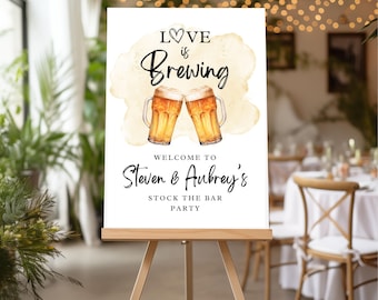 May include: A white sign with a watercolor background and the text "Love is Brewing" with two beer mugs clinking. The sign also says "Welcome to Steven & Aubrey's Stock the Bar Party".