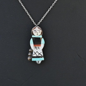 May include: A silver necklace with a pendant shaped like a stylized figure. The pendant is crafted from inlaid stones in white, black, turquoise, and red. The figure has a detailed face and hangs from a fine silver chain.