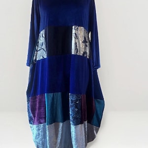 Könnte beinhalten: Ein langärmeliges Patchwork-Kleid in Blau-, Lila- und Silbertönen. Das Kleid hat einen runden Ausschnitt und eine lockere, fließende Silhouette. Das Patchwork-Design umfasst Samt- und gemusterte Stoffe und schafft einen einzigartigen und künstlerischen Look.