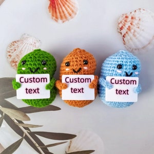 May include: Three crocheted plush toys holding signs with the text "Custom text". The toys are green, orange, and blue.