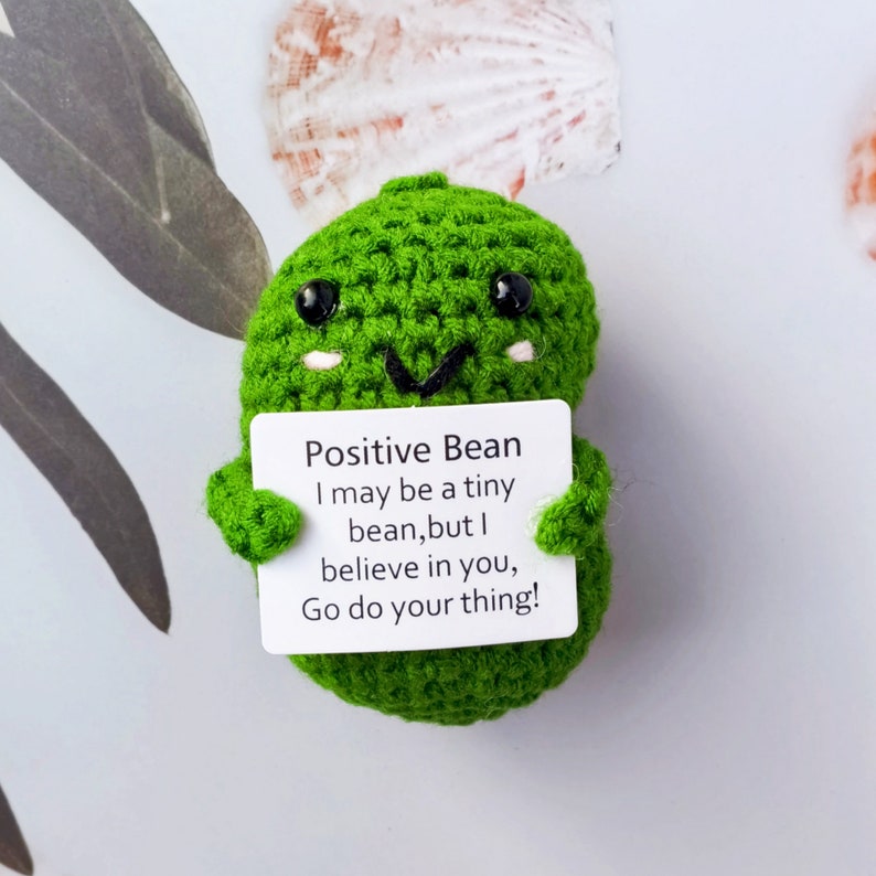 May include: A green crocheted bean plush toy holding a white card with the text "Positive Bean I may be a tiny bean, but I believe in you, Go do your thing!"