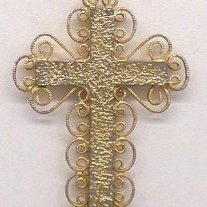 Peut inclure: Pendentif croix en filigrane doré. La croix présente un centre texturé et des bords en filigrane ornés et tourbillonnants. Une petite boucle dorée est située en haut pour la suspension. Le pendentif est probablement en métal et est conçu pour être porté comme bijou.