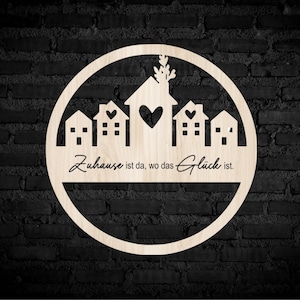 May include: A wooden circle with a cutout design of houses and a heart. The text "Zuhause ist da, wo das Glück ist." is written below the houses.