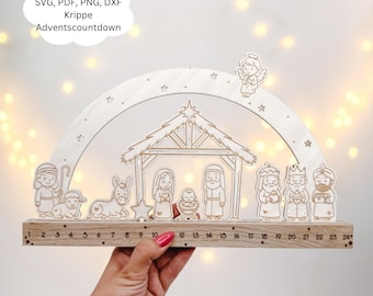 May include: A wooden Advent calendar depicting a nativity scene with figures and a countdown from 1 to 24. The design includes a stable, angel, and star, with the text "Laserdatei SVG, PDF, PNG, DXF Krippe Adventscountdown".