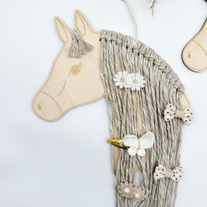 Pu&ograve; includere: Testa di cavallo in legno con una lunga criniera di filato beige. La criniera &egrave; decorata con fermagli per capelli a forma di fiori bianchi e marroni, fermagli per capelli a forma di farfalla bianca e fermagli per capelli a pois marroni.