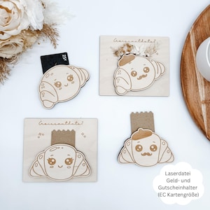 Könnte beinhalten: Lasergeschnittene Kartenhalter in Croissantform aus Holz mit niedlichen Gesichtern. Einige Halter haben eine Karte eingesetzt. Die Halter befinden sich auf einer hellen Holzoberfläche mit getrockneten Blumen und Text.