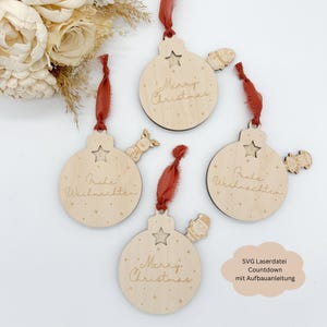 May include: Set of five wooden Christmas ornament countdown decorations with red ribbon. The ornaments are round and feature the text "Merry Christmas", "Frohe Weihnachten" and a star.