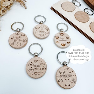 Op de afbeelding: Een verzameling houten sleutelhangers met zilveren ringen. Elke sleutelhanger heeft gegraveerde ontwerpen en tekst, waaronder zinnen als "YOU ARE BOOTY-FUL!" en "I LIKE YOU." De sleutelhangers zijn rond en van licht hout.