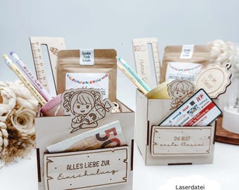 Puede incluir: Dos cajas de regalo de madera llenas de útiles escolares, incluyendo lápices, reglas y pequeñas bolsas. Una caja tiene un billete de 50 euros y el texto "ALLES LIEBE ZUR Einschulung". La otra caja tiene una tarjeta de regalo y el texto "DU BIST erste Klassi".