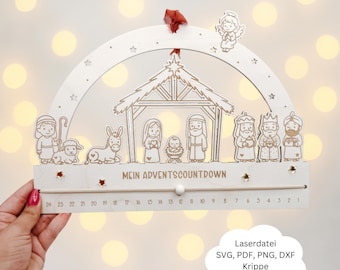 May include: A wooden Advent countdown calendar with a nativity scene design, including figures and a countdown slider. The design features a stable, stars, and an angel. The text "MEIN ADVENTSCOUNTDOWN" is visible. The calendar is held by a hand.
