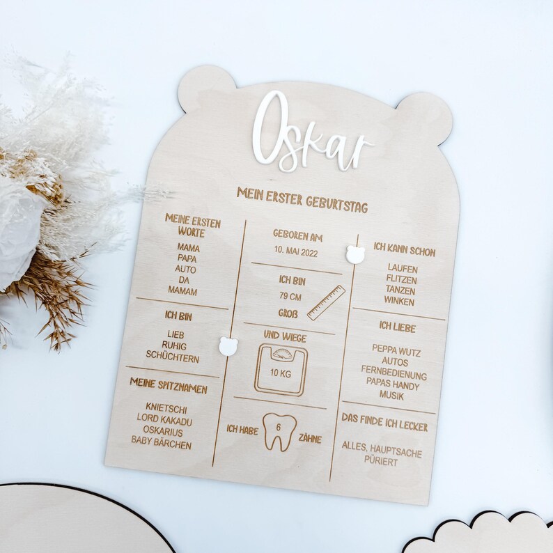 Puede incluir: Un letrero de madera con forma de oso, celebrando el primer cumplea&ntilde;os de un ni&ntilde;o. El letrero est&aacute; personalizado con el nombre "Oskar" e incluye detalles como la fecha de nacimiento, la altura, el peso, las primeras palabras, las cosas favoritas y un gr&aacute;fico de dientes.