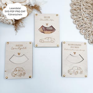 May include: Three wooden gift card holders with car designs. Each has a cash cutout and engraved text and car illustrations. The holders are fastened with gold-coloured rivets. The text includes phrases in German.