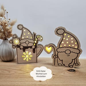 May include: Two wooden Christmas gnome figures with light-up features. The gnome on the left is holding a mug with a snowflake and candy cane. The gnome on the right is holding a heart-shaped stick. The text "SVG Datei Wichtel zum Hinstellen" is visible at the bottom of the image.