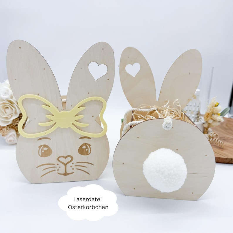 May include: Two wooden bunny shaped Easter baskets. One bunny has a yellow bow and a face. The other bunny has a white pom-pom tail.  The text "LaserdDatei Osterk&ouml;rbchen" is at the bottom of the image.