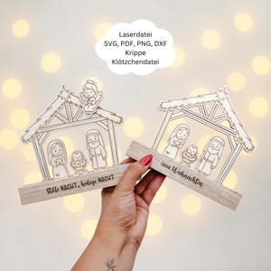 May include: Two wooden nativity scene ornaments. Each features a laser-cut design of a stable with Mary, Joseph, and baby Jesus. One reads "Stille Nacht, heilige Nacht," the other "Frohe Weihnachten."