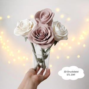 Può includere: Un piccolo vaso di vetro che contiene un bouquet di rose artificiali. Il bouquet comprende due rose bianche e due rose malva con steli e foglie verdi. L'immagine ha uno sfondo morbido e sfocato con luci bokeh.