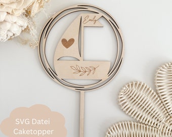 May include: Wooden cake topper with a sailboat design, a heart, and leaves. The topper is personalized with the name "Emily".
