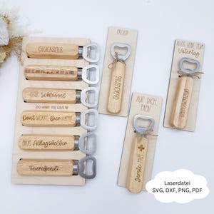 Könnte beinhalten: Holz-Flaschenöffner mit silberfarbenen Öffnern. Einige Öffner werden auf einem Holzhalter präsentiert, andere auf einzelnen Karten. Auf den Öffnern stehen Texte wie "Don't Worry, Bier Happy" und "Glückspils".