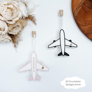 Könnte beinhalten: Zwei Flugzeug-Geldhalter mit Glasröhren und Korken. Einer ist weiß und schwarz, der andere rosa und weiß mit Text. Auf jedem Flugzeug befindet sich ein kleines Herz. Der Text "3D Druckdatei Geldgeschenk" befindet sich in einer Sprechblase.