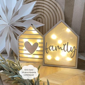 Op de afbeelding: Twee houten lichtgevende huisjes met een hart en het woord "familie" uitgesneden. De huisjes zijn verlicht met warmwitte LED-lampjes. De huisjes staan op een houten oppervlak.