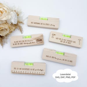 Puede incluir: Cinco niveles de madera con mensajes grabados y viales de burbujas verdes. Los niveles son de color marrón claro. Un nivel tiene una regla grabada. También aparece el texto "Laserdatei SVG, DXF, PNG, PDF".