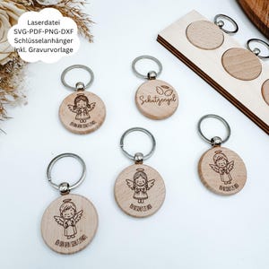 Könnte beinhalten: Schlüsselanhänger aus Holz mit Engelsmotiven. Jeder runde Schlüsselanhänger hat eine gravierte Engel-Illustration und Text. Die Schlüsselanhänger haben silberfarbene Schlüsselringe. Der Text auf den Schlüsselanhängern lautet "Schutzengel" und "ICH BIN DEIN SCHUTZENGEL".