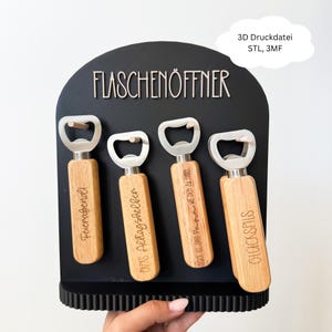 Könnte beinhalten: Eine schwarze Wandhalterung für Flaschenöffner mit vier Flaschenöffnern aus Holz. Jeder Öffner hat einen silbernen Metallöffner und ist mit deutschem Text graviert. Das Display trägt auch den Text "FLASCHENÖFFNER".
