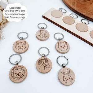 Könnte beinhalten: Holz-Schlüsselanhänger mit eingravierten Tierdesigns, darunter ein Fuchs, ein Bär, ein Löwe, ein Pferd, ein Kaninchen und ein Dinosaurier. Jeder Schlüsselanhänger hat einen silbernen Ring. Der Text "Laserdatei SVG-PDF-PNG-DXF Schlüsselanhänger inkl. Gravurvorlage" ist sichtbar.