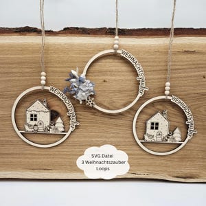 Könnte beinhalten: Drei Weihnachts-Ornamente aus Holz mit dem Text "Weihnachtszauber" in einem Kreis. Jedes Ornament zeigt ein anderes Design: ein Haus, einen Baum und eine Schneeflocke.