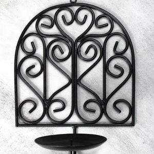 May include: Black metal candle holder with a decorative scroll design. The holder has a round candle cup and a hook for hanging.