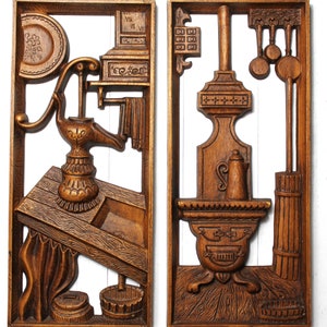 May include: A pair of wooden wall plaques depicting scenes from a kitchen. The left plaque features a hand-carved wooden pump with a sink and a shelf with a clock. The right plaque features a hand-carved wooden stove with a kettle and a rack of kitchen utensils.