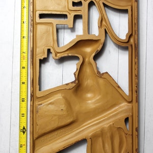 May include: A gold-coloured metal wall decor with a cutout design. The design features a series of abstract shapes and curves. The decor is approximately 17 inches tall.