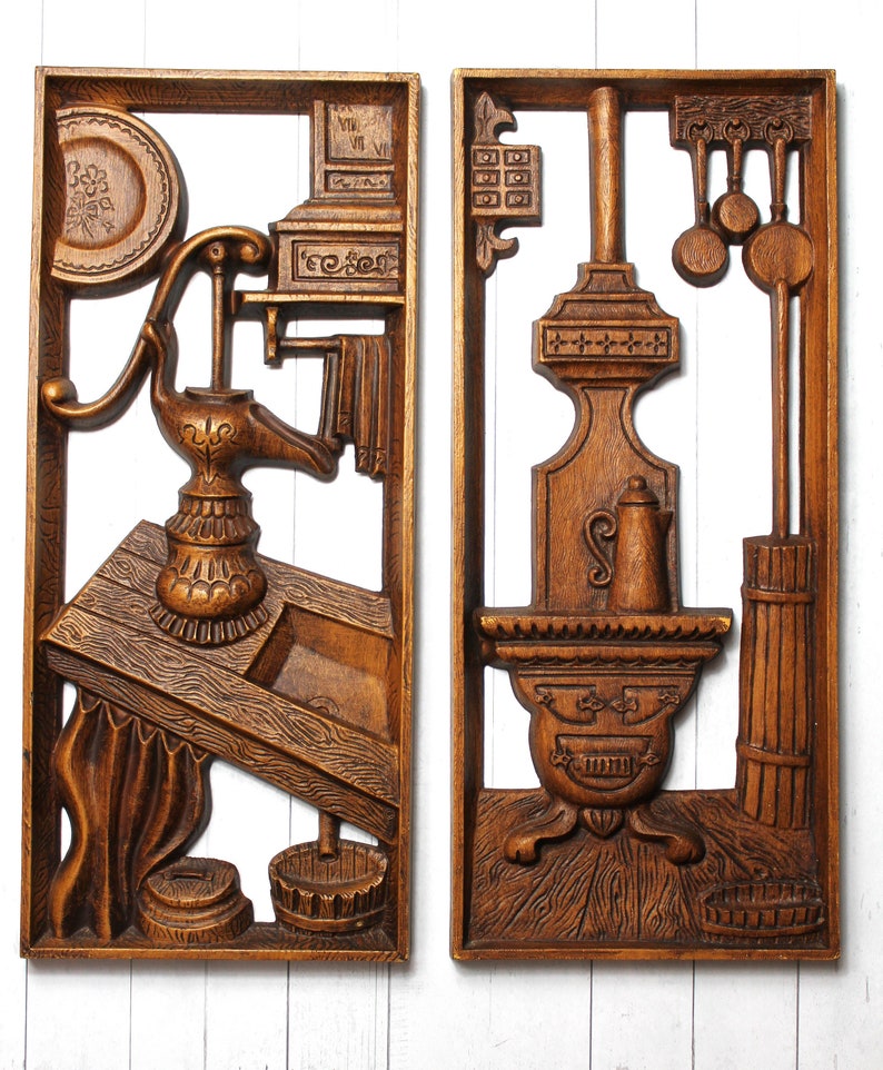 May include: A pair of wooden wall plaques depicting scenes from a kitchen. The left plaque features a hand-carved wooden pump with a sink and a shelf with a clock. The right plaque features a hand-carved wooden stove with a kettle and a rack of kitchen utensils.