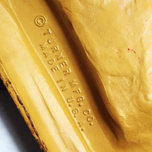 May include: Close-up of a gold-coloured metal object with the text "&copy; TURNER MFG. CO. MADE IN U.S.A." embossed on the surface.