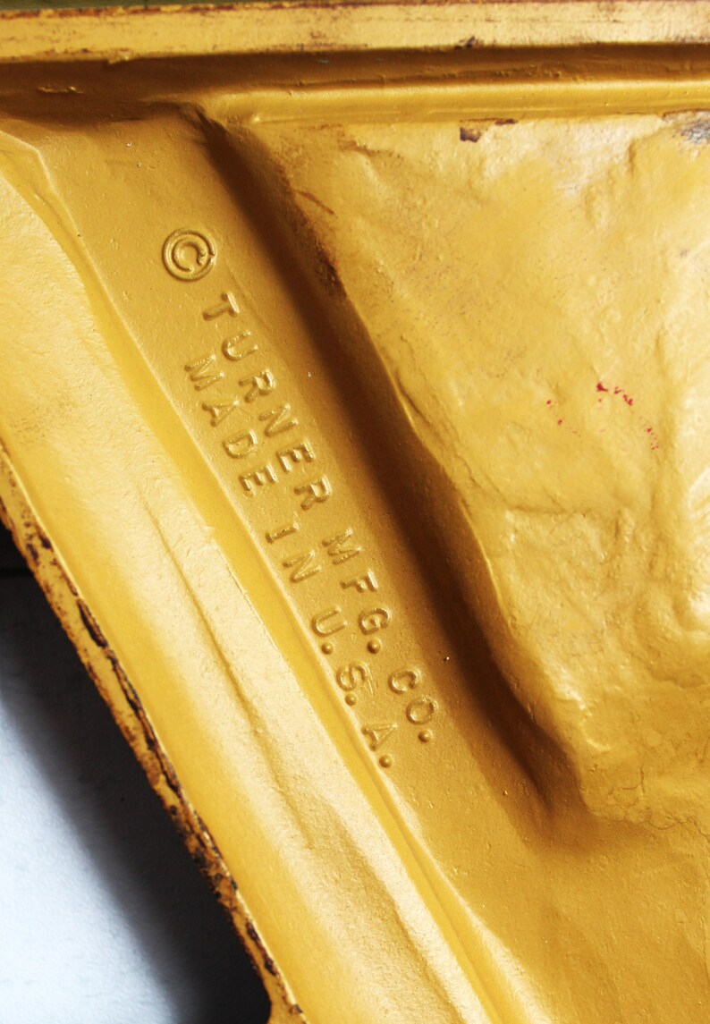 May include: Close-up of a gold-coloured metal object with the text "&copy; TURNER MFG. CO. MADE IN U.S.A." embossed on the surface.