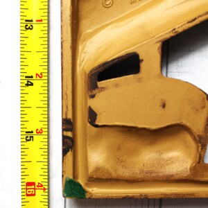 May include: A yellow metal doorstop with a green edge. The doorstop is shaped like a stylised human figure. The text "&copy; TURNER MFG. MADE IN U.S.A." is visible on the doorstop.
