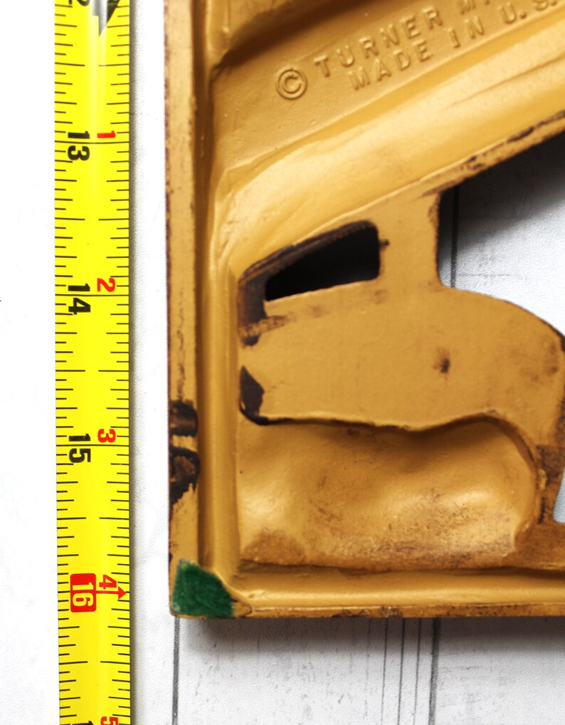 May include: A yellow metal doorstop with a green edge. The doorstop is shaped like a stylised human figure. The text "&copy; TURNER MFG. MADE IN U.S.A." is visible on the doorstop.