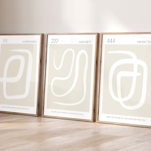 May include: Three framed prints with beige backgrounds and white abstract line drawings. The prints are labeled with the numbers 111, 222, and 444, and the words "Manifestation", "Alignment", and "Protection".