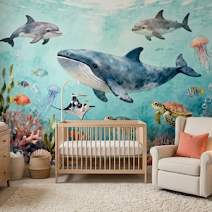 Op de afbeelding: Een kinderkamer met een oceaan-thema muurschildering met een walvis, dolfijnen, haaien en andere zeedieren. Een houten wieg, commode en fauteuil bevinden zich in de kamer. De kamer heeft een vloerkleed, gordijnen en een lamp.