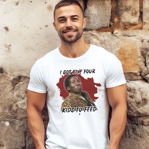 以下が含まれることがあります： 白地に赤と白のグラフィックがプリントされたTシャツ。グラフィックには男性が描かれており、"I got five four kids to feed."というテキストが書かれている