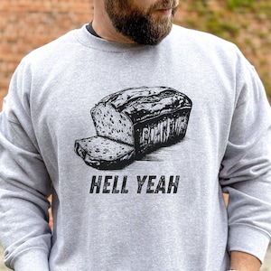 May include: A grey sweatshirt with a black and white illustration of a loaf of bread and the text "Hell Yeah".