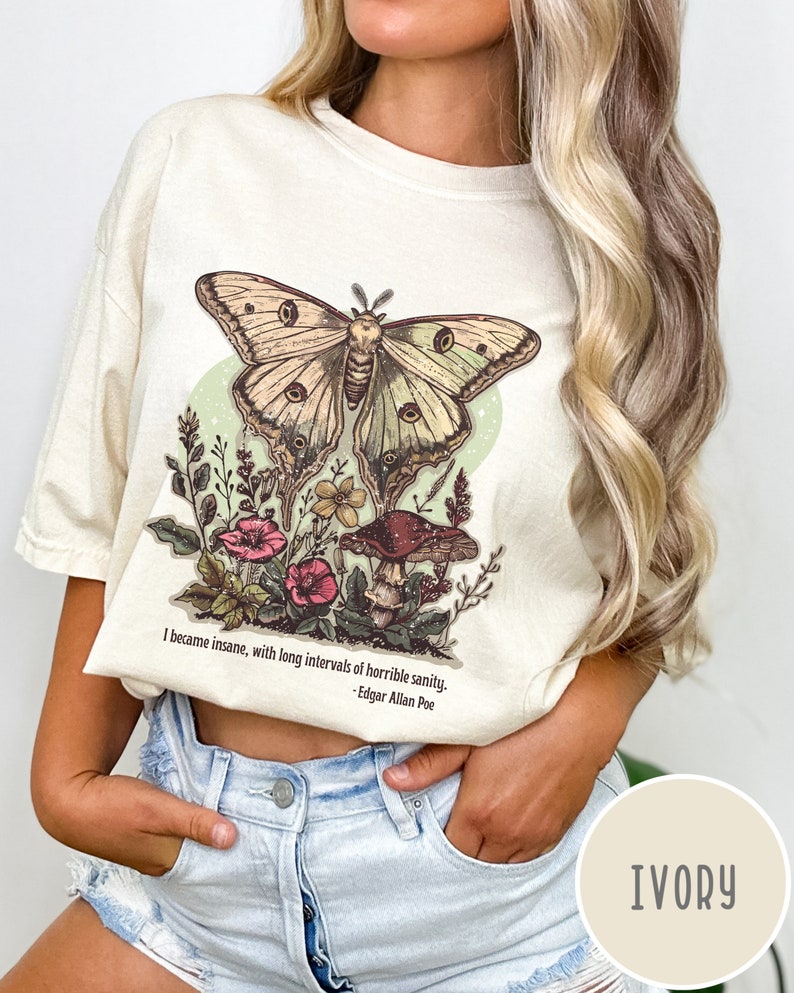 May include: A cream coloured t-shirt featuring a vintage illustration of a butterfly, mushrooms and flowers. The text "I became insane, with long intervals of horrible sanity. -Edgar Allan Poe" is printed on the shirt.