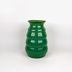 Peut inclure: Un vase en céramique vert brillant. Le vase a un design empilé et arrondi avec un dessus évasé. La couleur est un vert profond et vibrant, et le vase est posé sur un fond blanc.