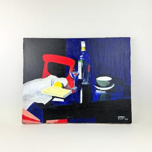 May include: Abstract still life painting featuring a red chair, a bottle, a glass, a bowl, and a book. The painting uses a dark blue and black background with a white tablecloth and a yellow lemon. The artwork is signed in the bottom right corner.