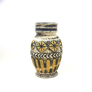 May include: A vintage ceramic vase with a textured surface. The vase features a cream-colored base with black and yellow geometric patterns. The rim is dark blue, and the overall design has a retro aesthetic.