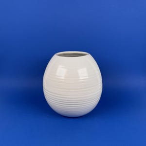 May include: A spherical white ceramic vase featuring a series of horizontal ridges or grooves encircling the body. The vase has a smooth, glossy finish and a wide, circular opening at the top, presenting a clean and simple design structure.