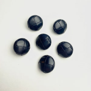 Può includere: Sei bottoni rotondi neri con un design intrecciato. I bottoni sono realizzati in un materiale strutturato e hanno una superficie leggermente rialzata.