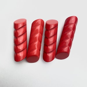 Può includere: Quattro bottoni di plastica rossa con un design attorcigliato. I bottoni sono lunghi circa 2,5 cm e hanno una finitura liscia e lucida.